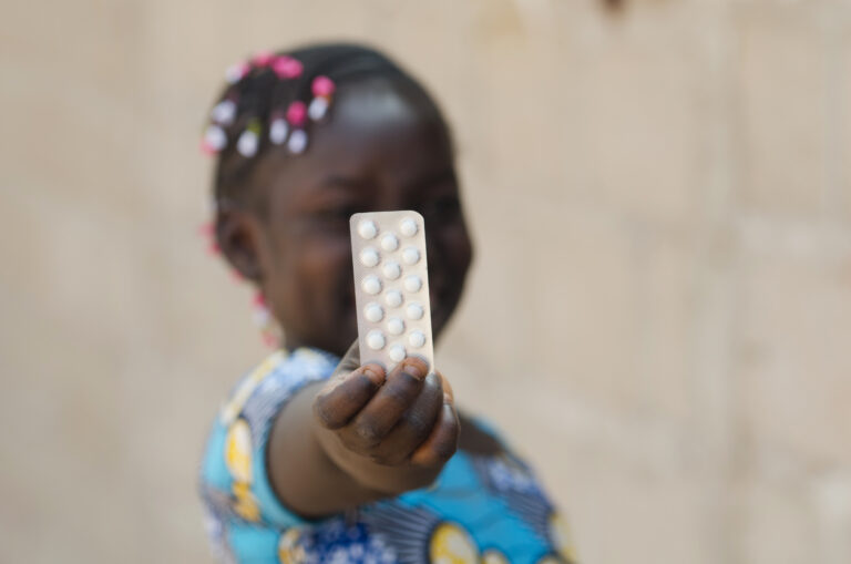 Young African girl holds up a package of birth control pills
